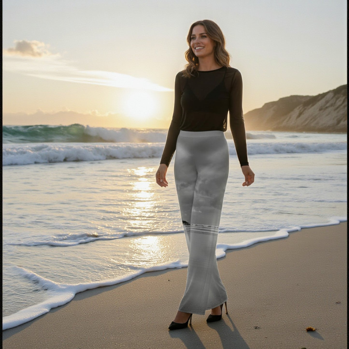 Woman standing on a beach at sunset wearing a black top and white pants.