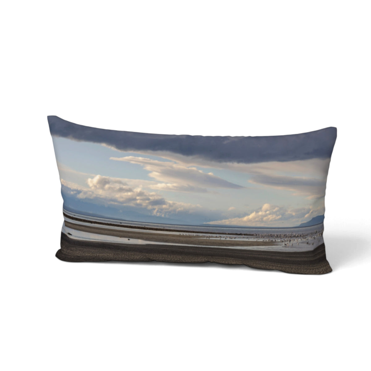 A rectangular lumbar throw pillow featuring a photographic print of a coastal landscape with dramatic clouds, a blue sky, and a dark shoreline, shown against a plain white background.