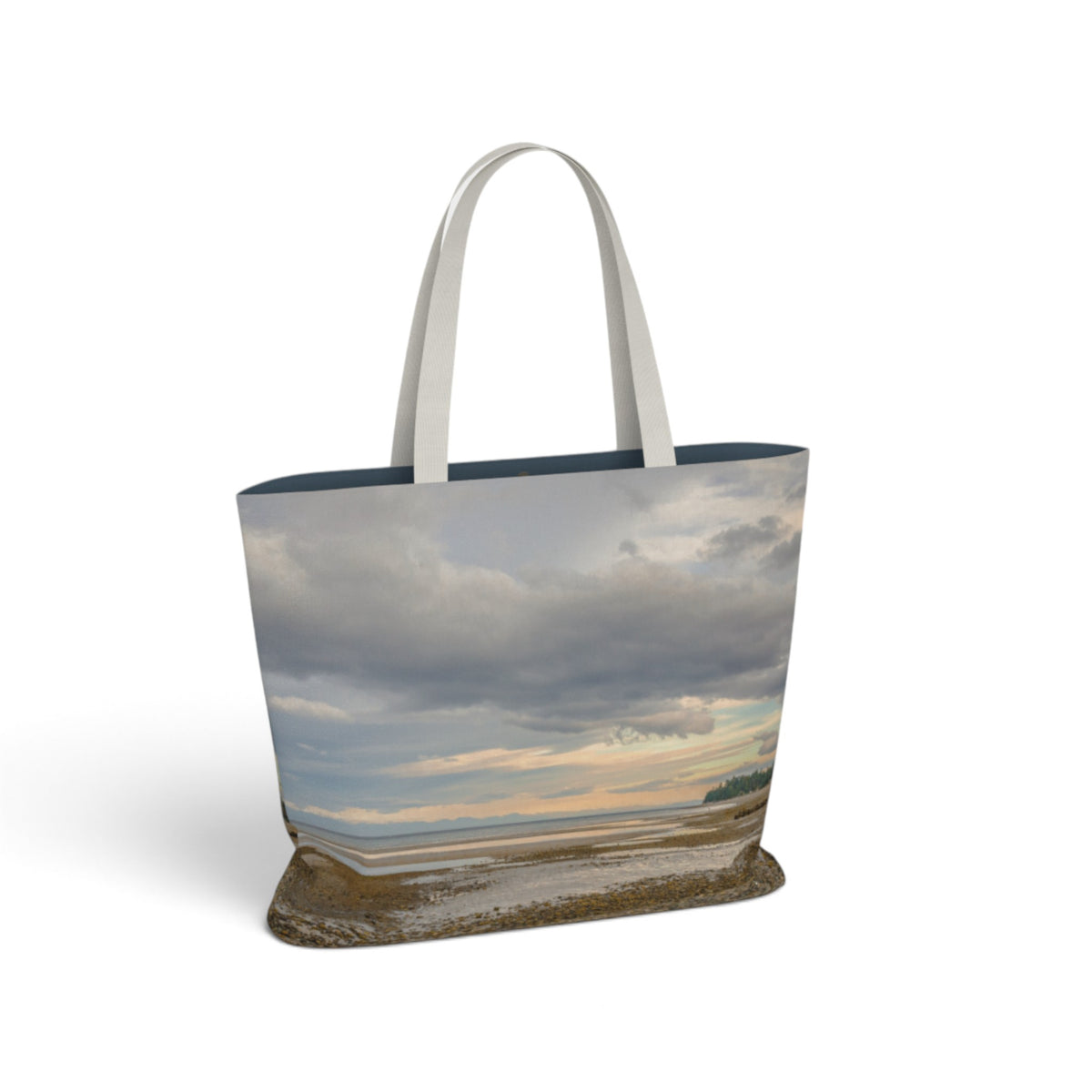 A tote bag featuring a photographic print of a coastal landscape with dramatic clouds, water, and a shoreline. The bag has light gray fabric shoulder straps and a dark navy blue inner lining, shown against a plain white background.