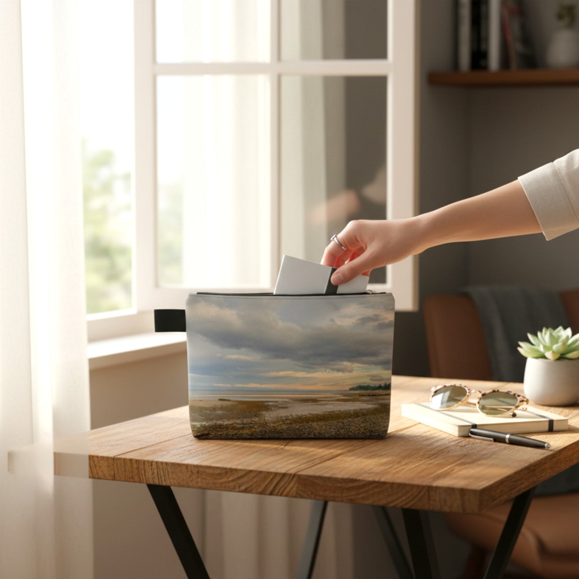 Person reaching into a pouch with a scenic design on a wooden table.