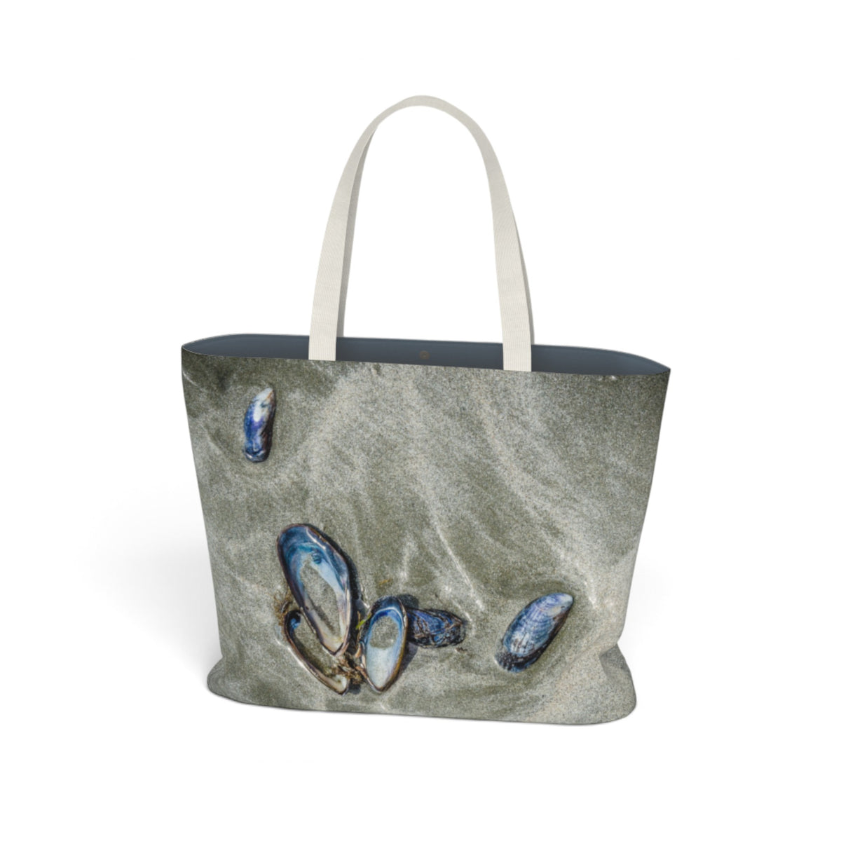 A tote bag featuring a printed design of blue abalone shells on a sandy beach, with off-white shoulder straps, shown against a plain white background.