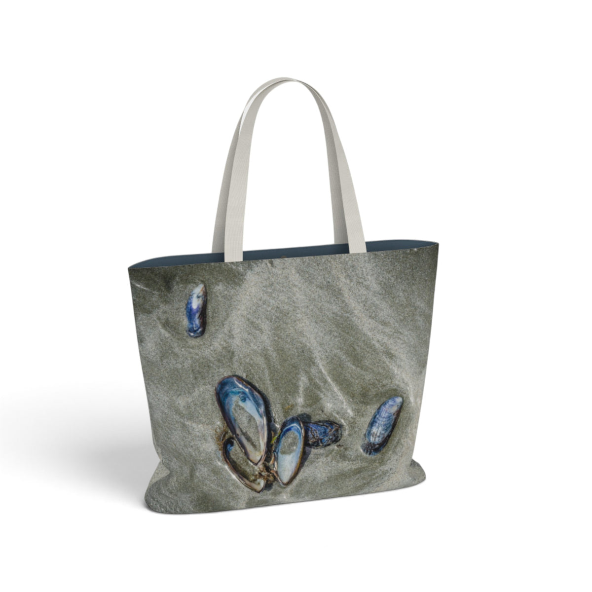 A canvas tote bag with a textured gray and blue seashell print, featuring off-white shoulder straps, shown on a clean white background.
