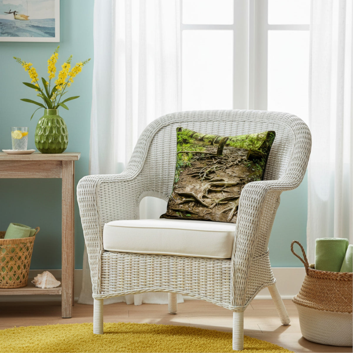 A white woven outdoor armchair with a cream cushion, styled in a bright room with a green forest print throw pillow, a side table, and a yellow side rug.