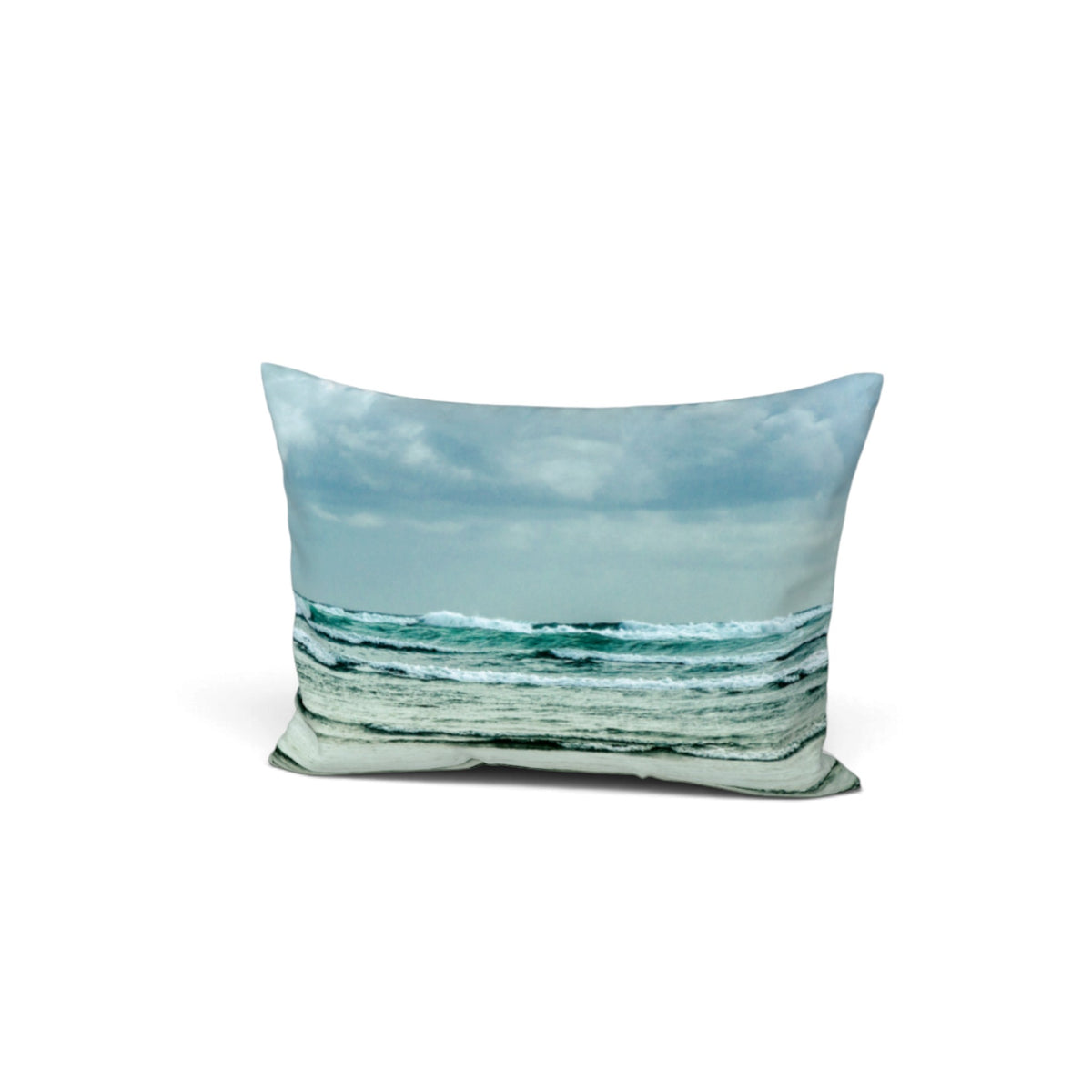 A rectangular throw pillow featuring a photographic print of a beach scene with ocean waves under a cloudy sky, shown against a plain white background.