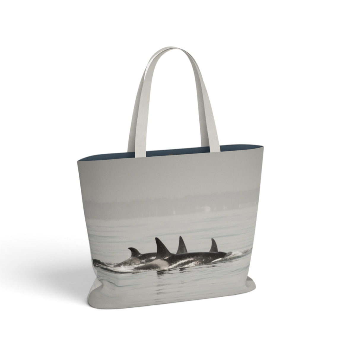 A tote bag featuring a grayscale photographic print of orcas surfacing from the water, with solid white shoulder straps and a dark navy blue inner lining, shown on a clean white background.