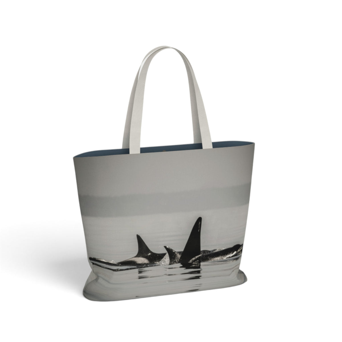 A tote bag featuring a grayscale photographic print of orcas in water, with white shoulder straps and a dark navy blue interior lining, shown on a clean white background.