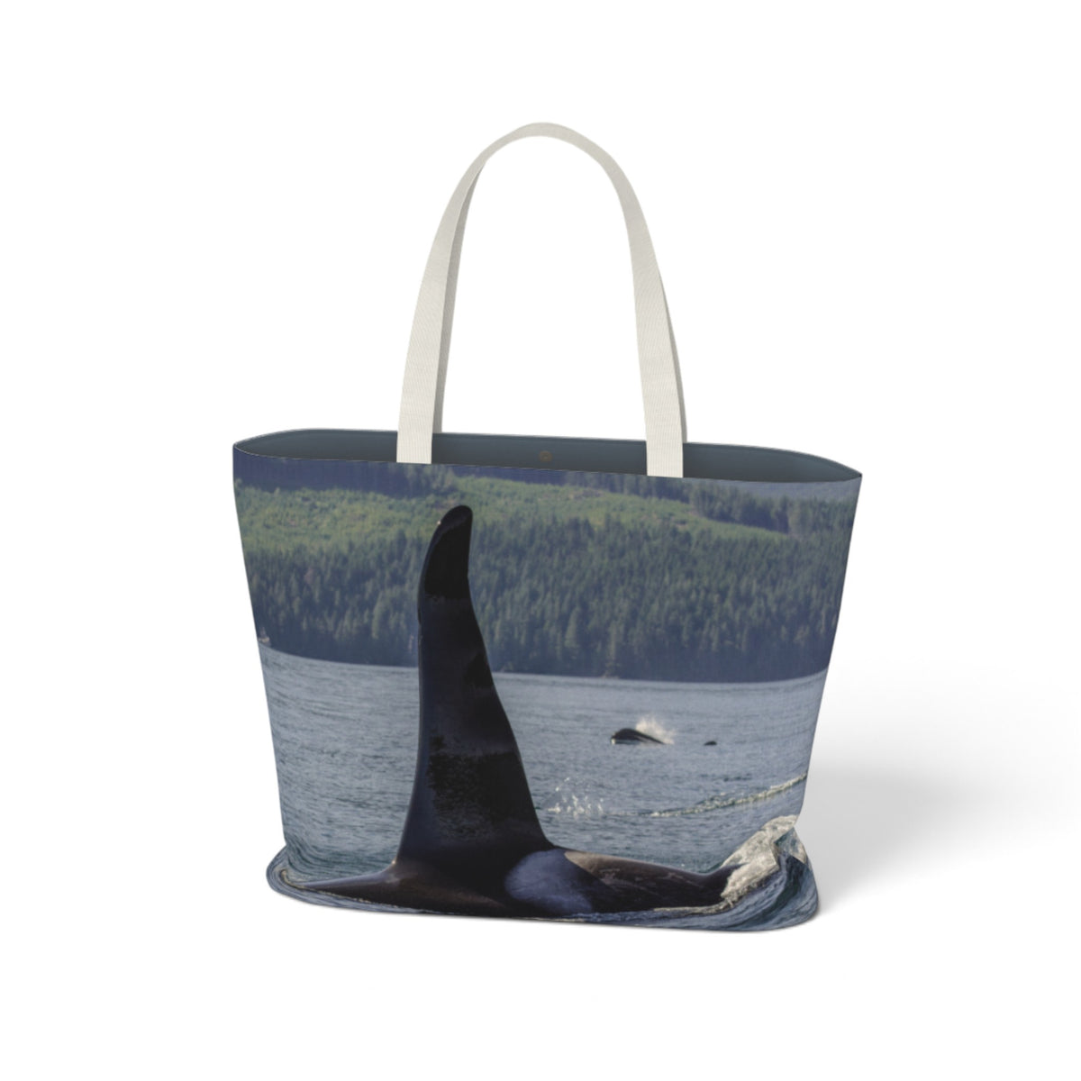 A tote bag with a photographic print of an orca whale in the water, featuring a forested shoreline in the background and white fabric handles, shown on a plain white background.