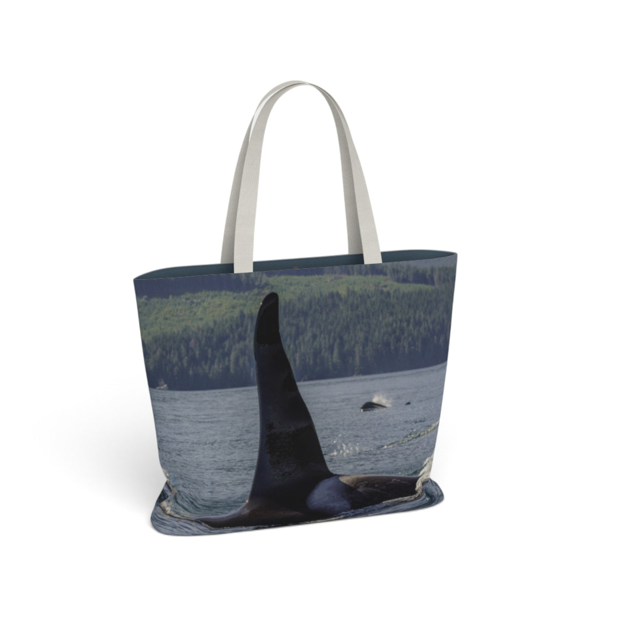 A tote bag with a photographic print of an orca whale in water, featuring a forested shoreline in the background and light gray fabric handles, shown on a plain white background.