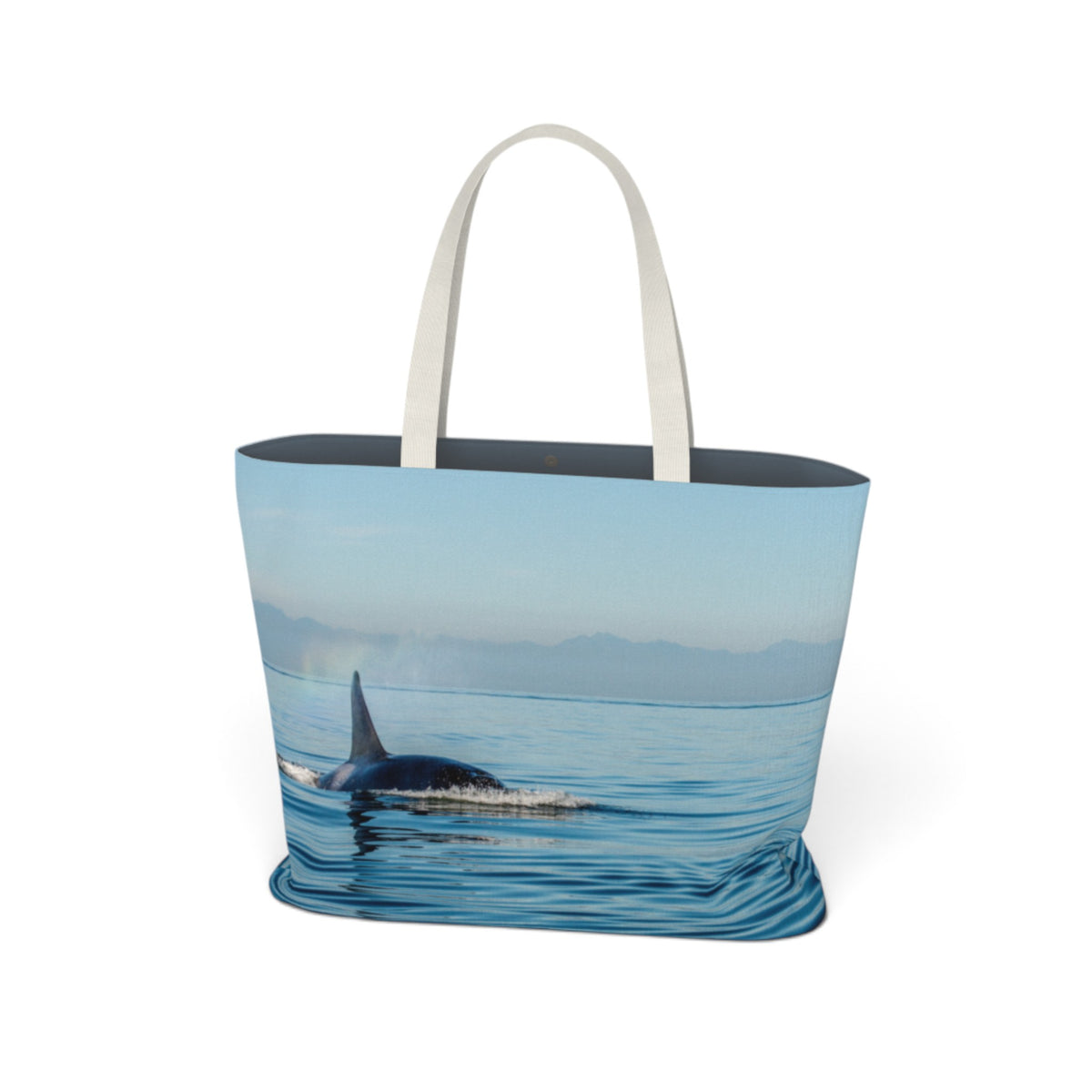 A tote bag with a photographic print of an orca whale in blue water, featuring light beige fabric handles and a dark navy blue interior lining, shown against a plain white background.