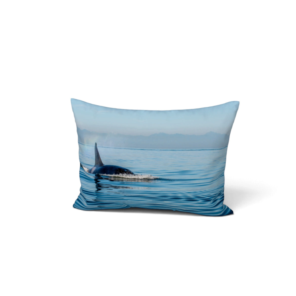 A rectangular decorative throw pillow featuring a photographic print of an orca whale surfacing in blue water with distant mountains under a pale sky, shown on a clean white background.