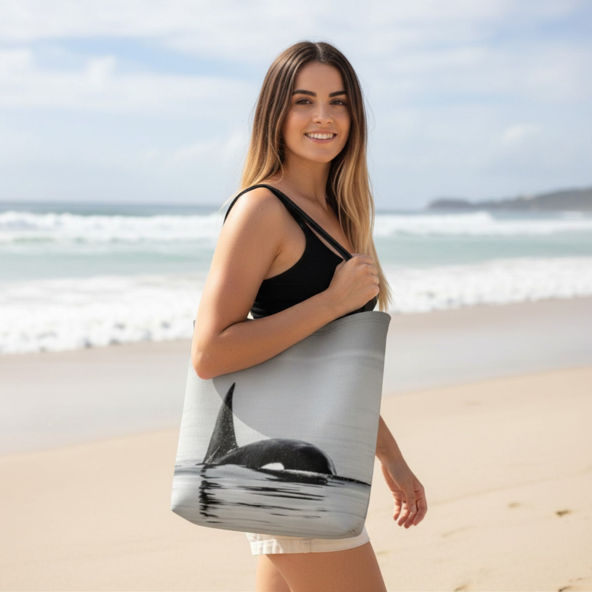 Woman holding a tote bag with an orca design on a beach