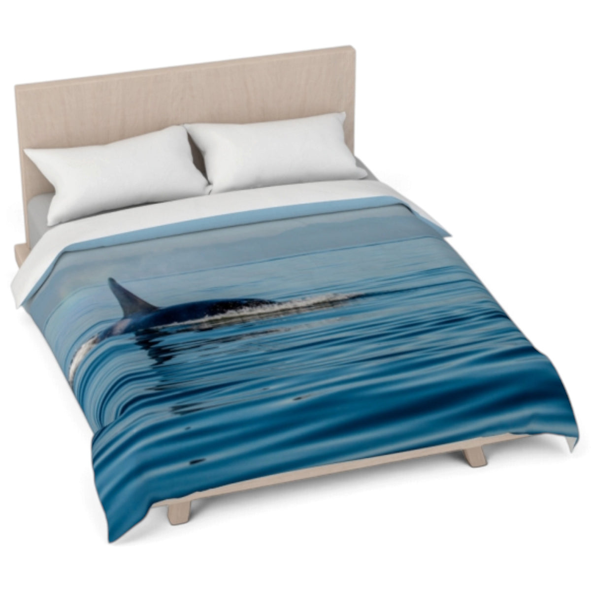 A bed dressed with a duvet cover featuring a blue whale surfacing in ocean water, styled with two white pillows and a light wood headboard against a white background.
