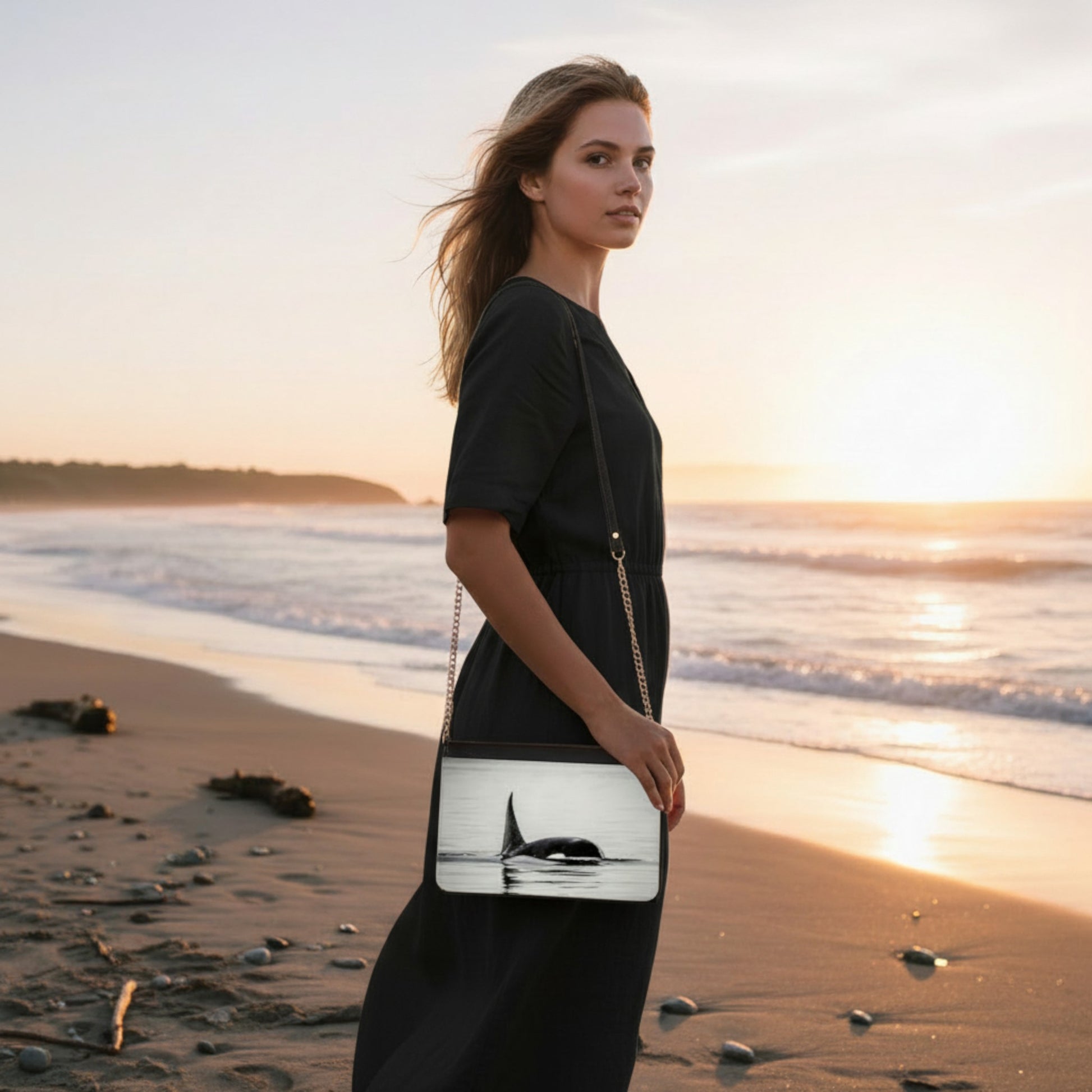 Woman holding a handbag with a whale design on a beach at sunset