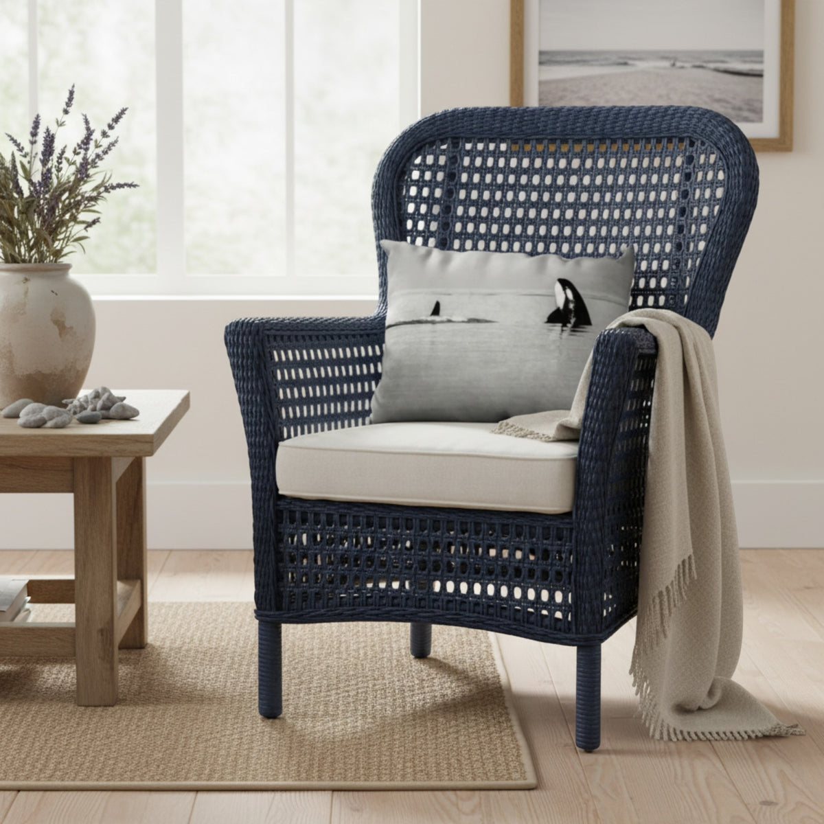 A navy blue wicker outdoor armchair with a cream cushion, styled with a gray pillow, a beige throw blanket, and set in a bright, modern living room next to a wooden side table.