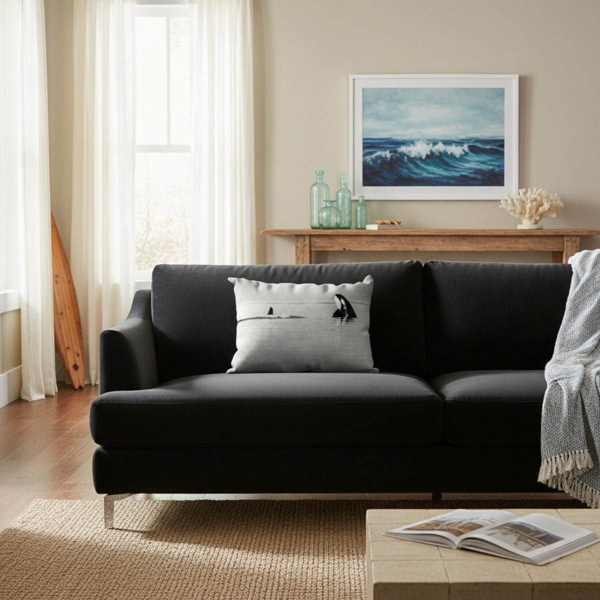 A modern black fabric sofa in a bright, contemporary living room, styled with a light gray pillow featuring a black bird silhouette, a wooden console table, and a framed ocean wave print on the wall.