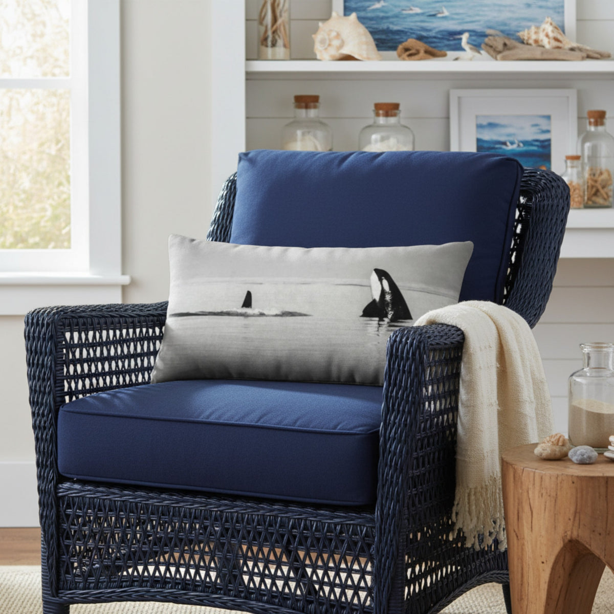 A navy blue woven outdoor armchair with matching navy cushions, styled with a gray pillow featuring an orca print and a cream throw blanket, set in a bright nautical-themed room.