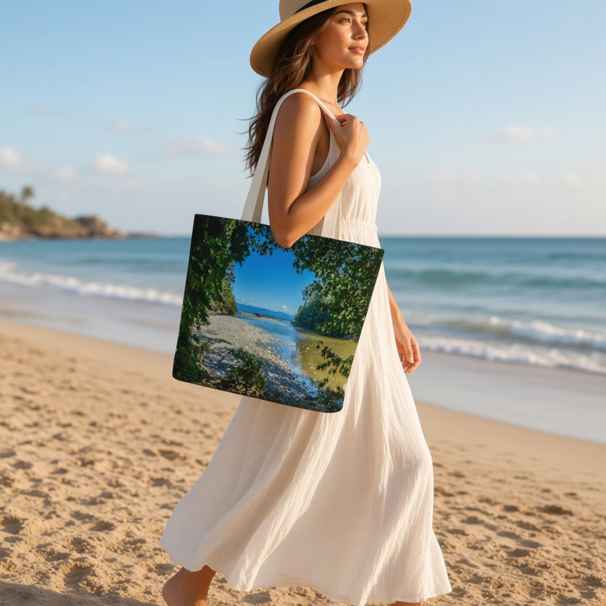 A woman in a white dress and straw hat walks on a sandy beach carrying a large tote bag printed with a scenic tropical beach landscape.