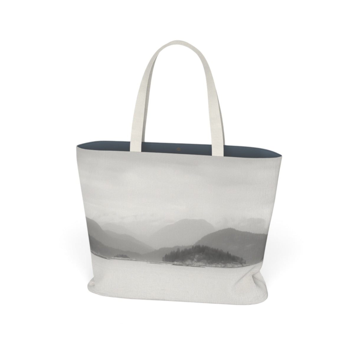 A canvas tote bag with a grayscale mountain landscape print on the front, featuring light beige handles and a dark navy blue interior lining, shown against a plain white background.