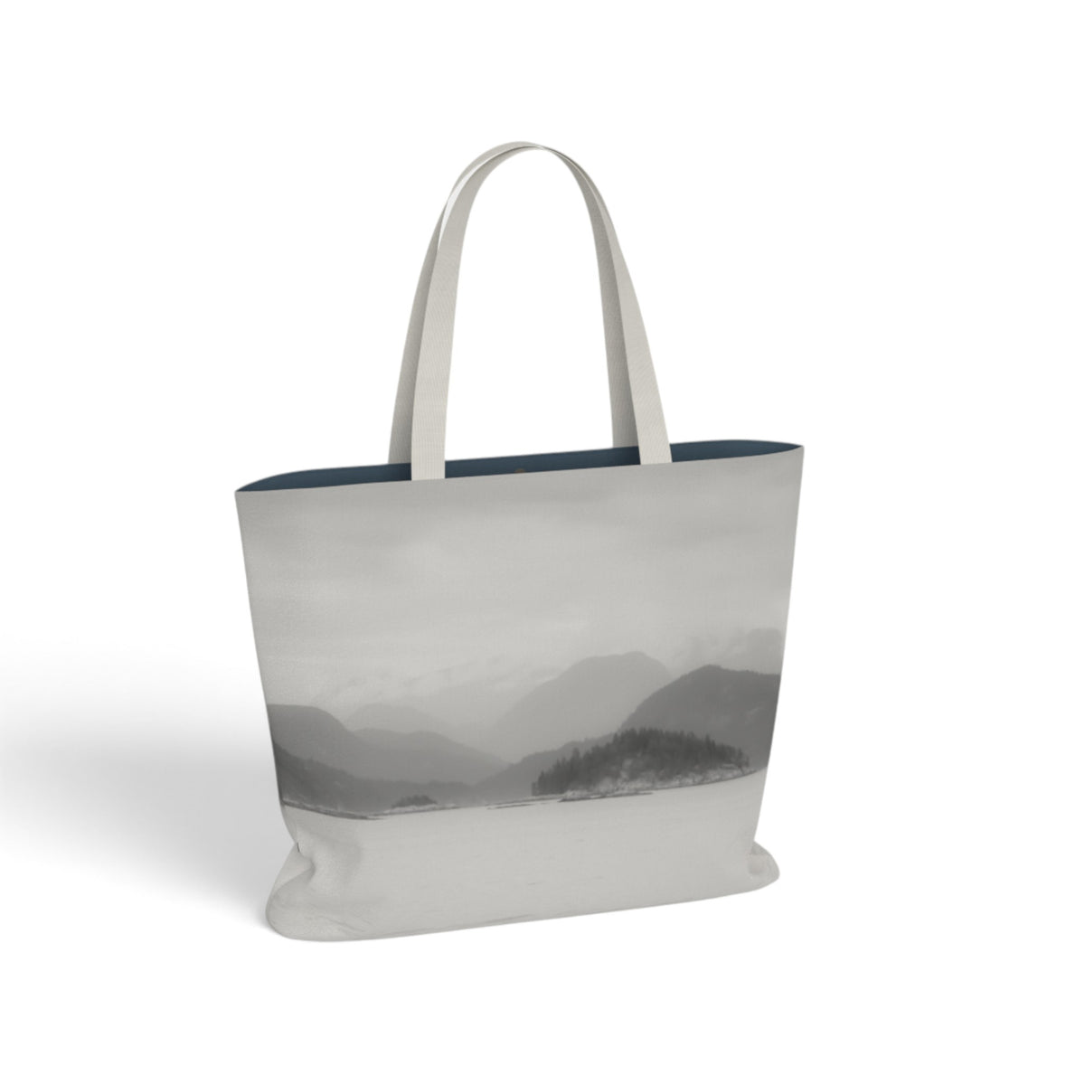 A canvas tote bag featuring a grayscale landscape print of misty mountains and a lake, with solid off-white shoulder straps and a dark navy blue interior lining, shown on a clean white background.