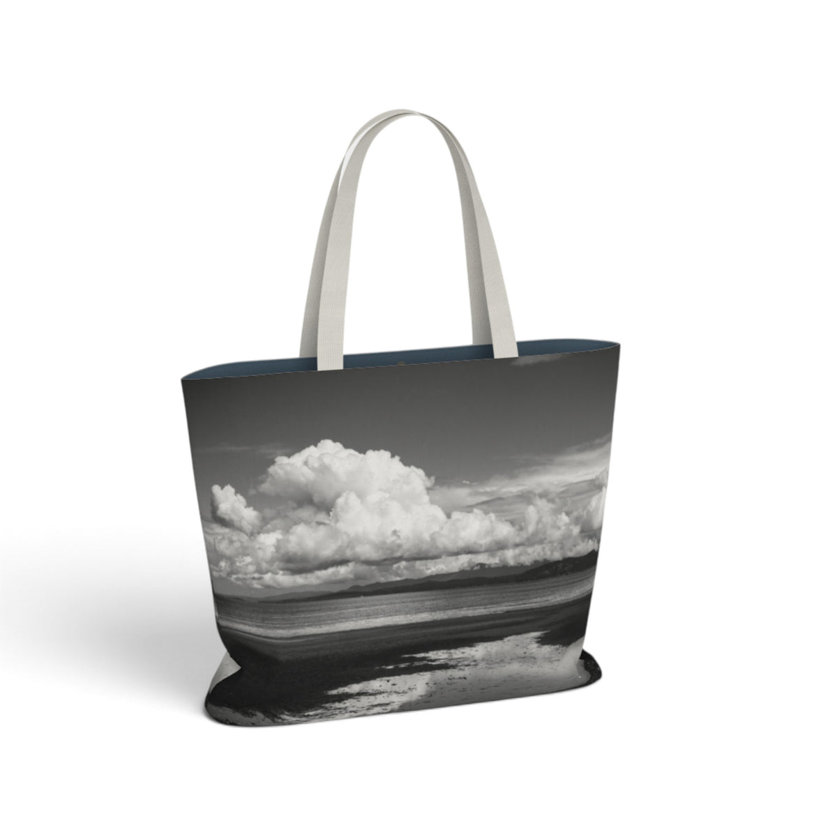 A tote bag featuring a black and white landscape photograph of a dramatic cloud formation over water, with light gray fabric handles, shown on a plain white background.