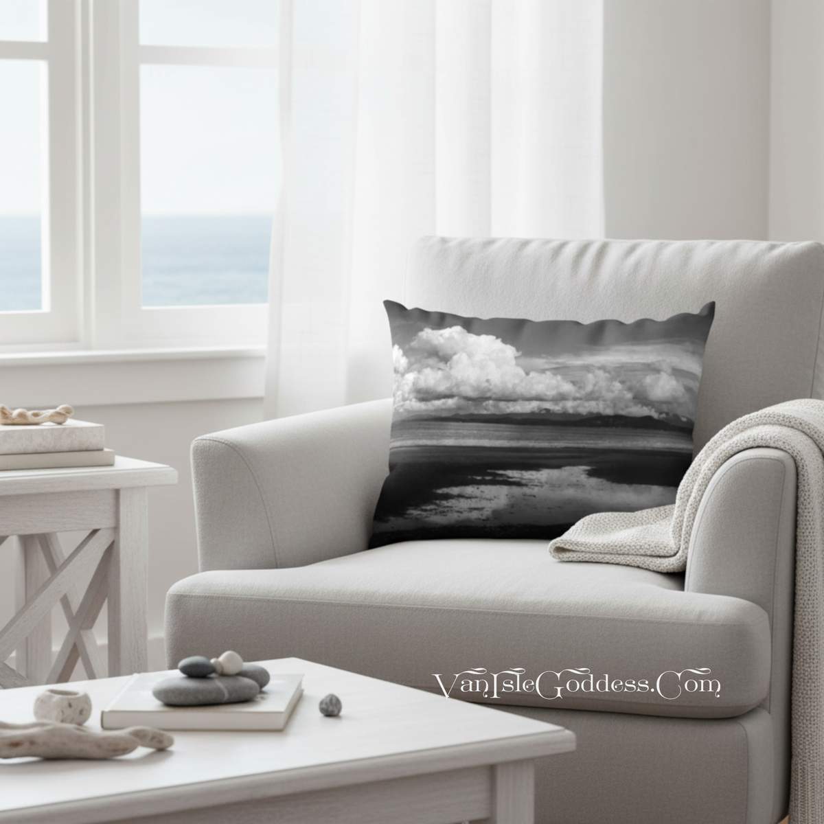 A square throw pillow with a black and white stormy sky and ocean print, resting on a light gray armchair in a bright, modern living room.