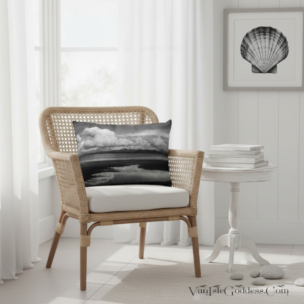 A black and white seashore landscape throw pillow displayed on a wicker armchair in a bright, modern room setting.