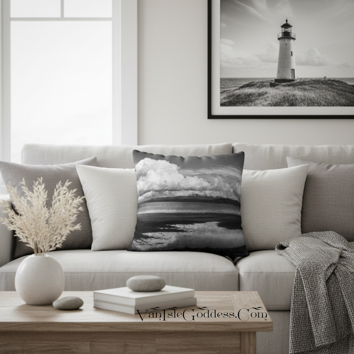 A square throw pillow with a black and white lighthouse landscape print is styled on a light beige sofa in a modern living room setting.