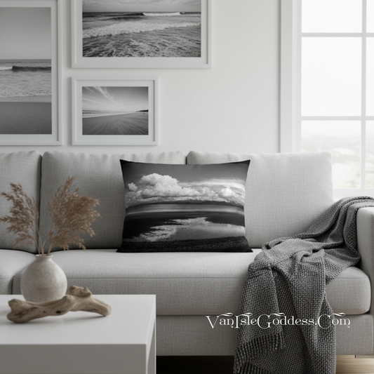 A square throw pillow featuring a black and white landscape photograph of a beach and clouds, styled on a light gray sofa in a modern living room setting.