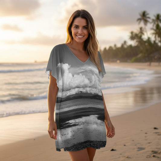 Woman wearing a dress with a beach and cloud design on a beach at sunset.