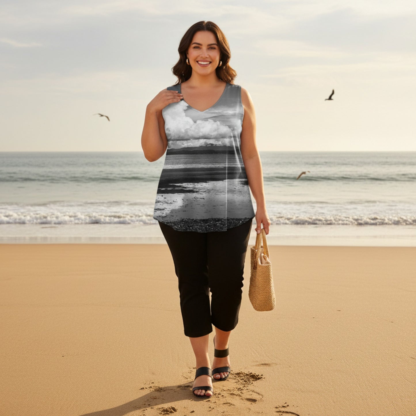 Woman standing on a beach wearing a sleeveless top with a beach scene print.