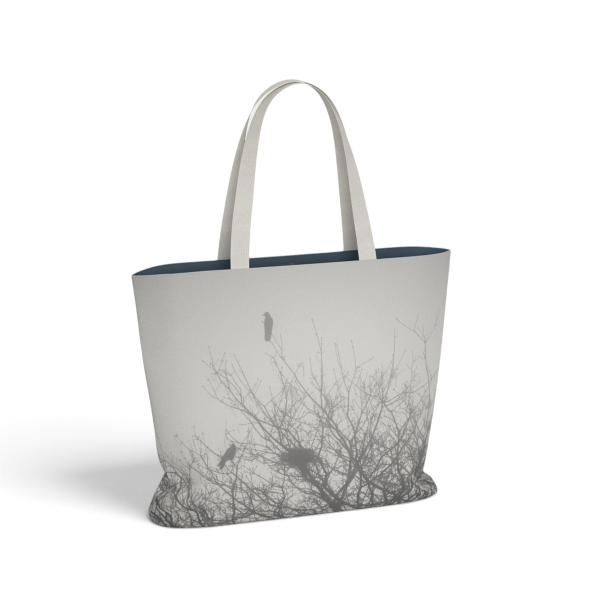 A tote bag with a light gray and white photographic print of crows perched in leafless trees, featuring light gray fabric shoulder straps and a dark navy blue interior lining, shown on a white background.