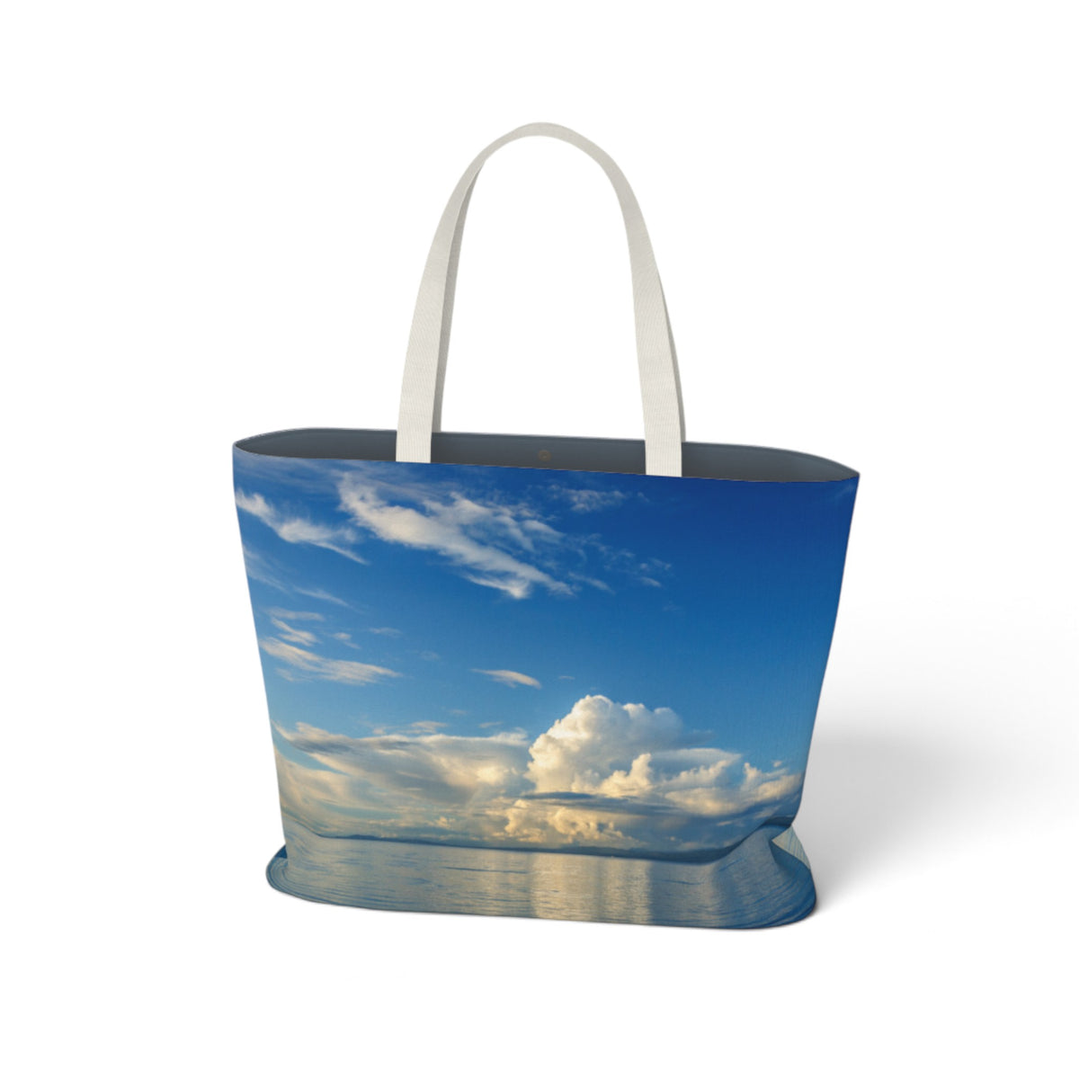 A tote bag featuring a printed scenic photograph of a blue sky with white clouds and water reflections, complete with two white shoulder straps, shown on a clean white background.