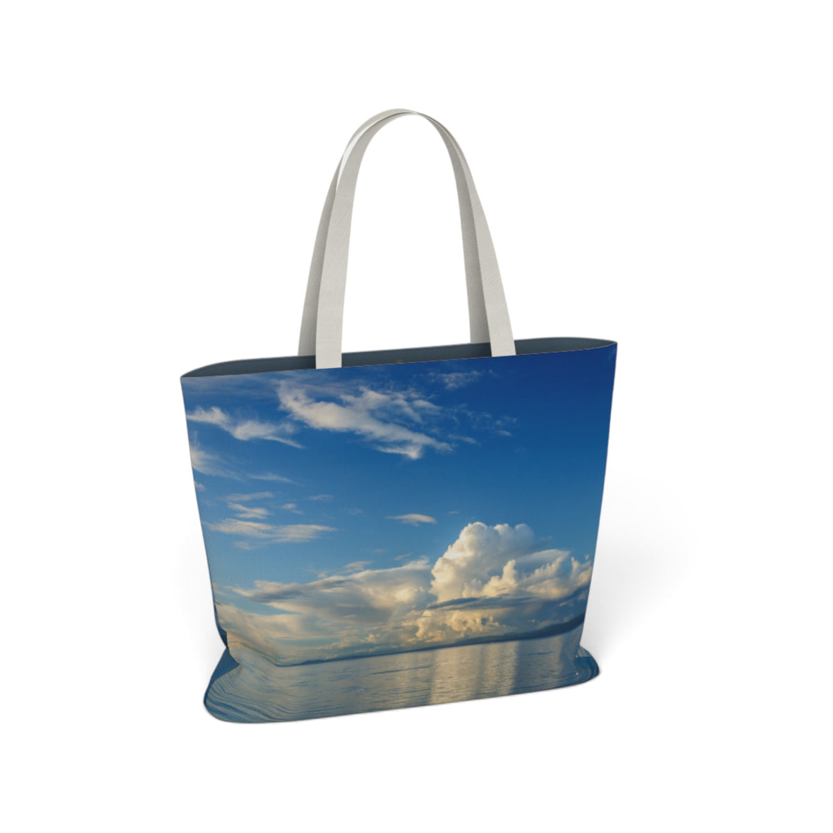 A tote bag featuring a scenic print of a blue sky with white clouds and water reflections, complete with light gray fabric handles, shown on a plain white background.