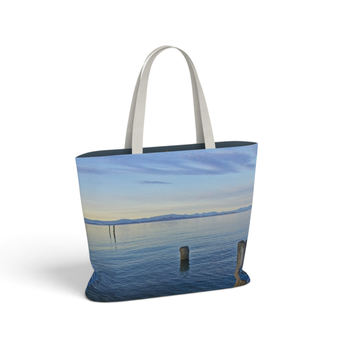 A tote bag featuring a scenic print of a calm lake with distant mountains under a blue sky, with light gray fabric shoulder straps, shown on a white background.