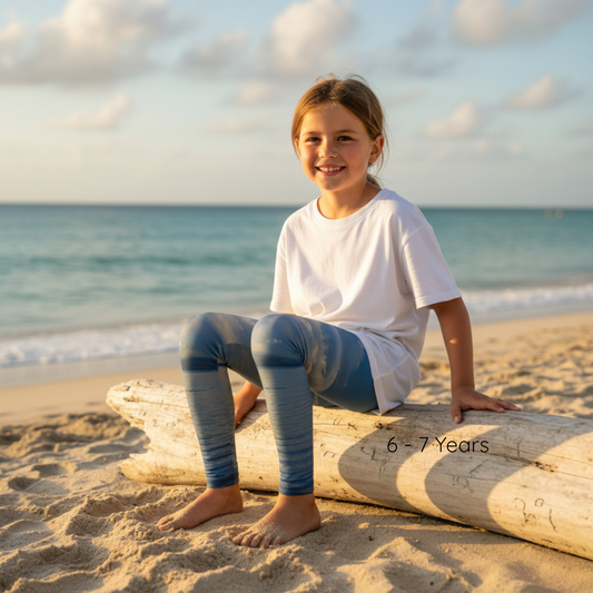 Young girl sitting on a log at the beach with ocean and sky in the background