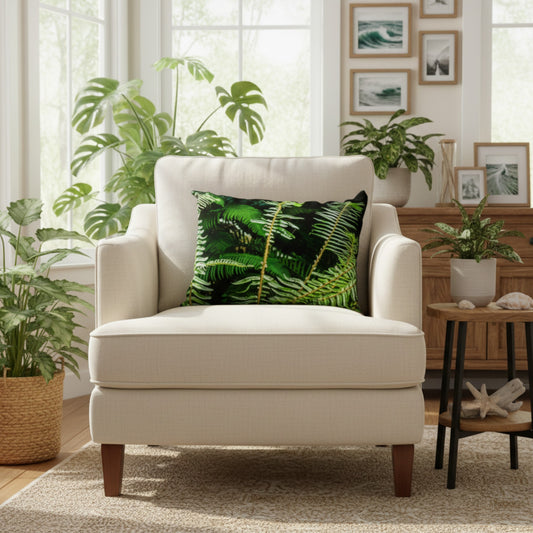 A cream upholstered accent chair in a bright, modern living room setting, styled with a green fern-patterned throw pillow. The chair is positioned on a textured beige rug next to a small wooden side table with plants and framed wall art.