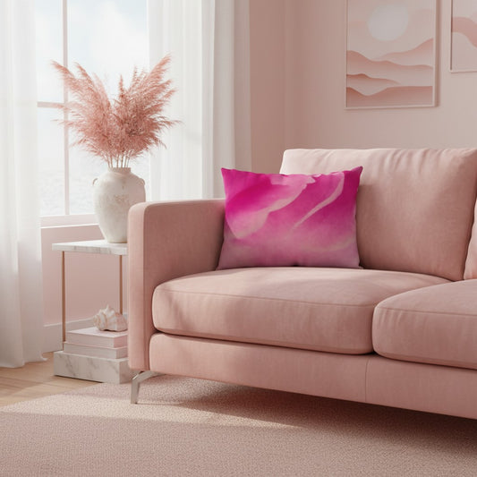 A pink throw pillow with a vibrant magenta and pink watercolor-style abstract pattern, styled on a dusty pink sofa in a softly lit living room.