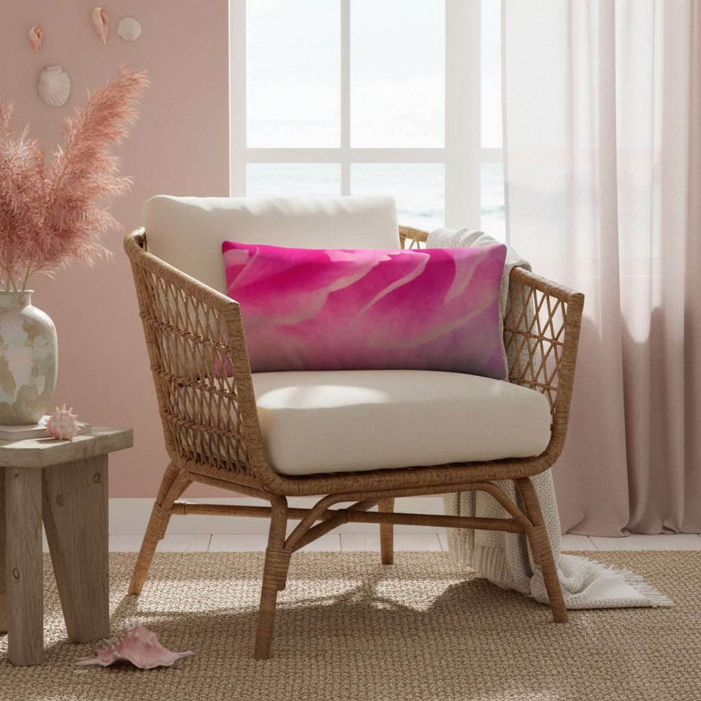 A woven rattan armchair with cream cushions in a bright coastal-style room, styled with a pink and purple abstract print throw pillow.
