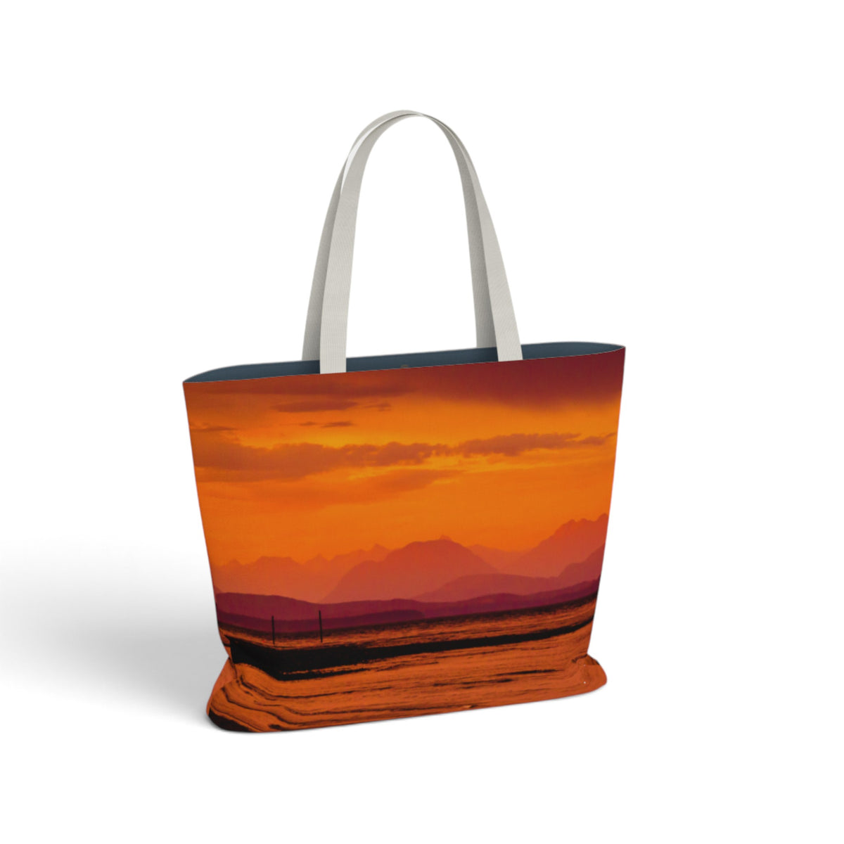 A tote bag featuring a vibrant orange and red sunset landscape print, with white shoulder straps, shown on a clean white background.