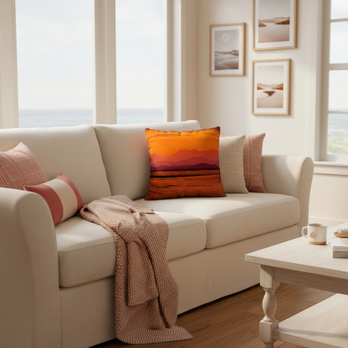 A cream-colored fabric sofa in a bright, modern living room setting, styled with a vibrant orange and pink striped throw pillow, a pink and white striped pillow, a beige textured pillow, a beige knit throw blanket, and a light wood coffee table nearby.