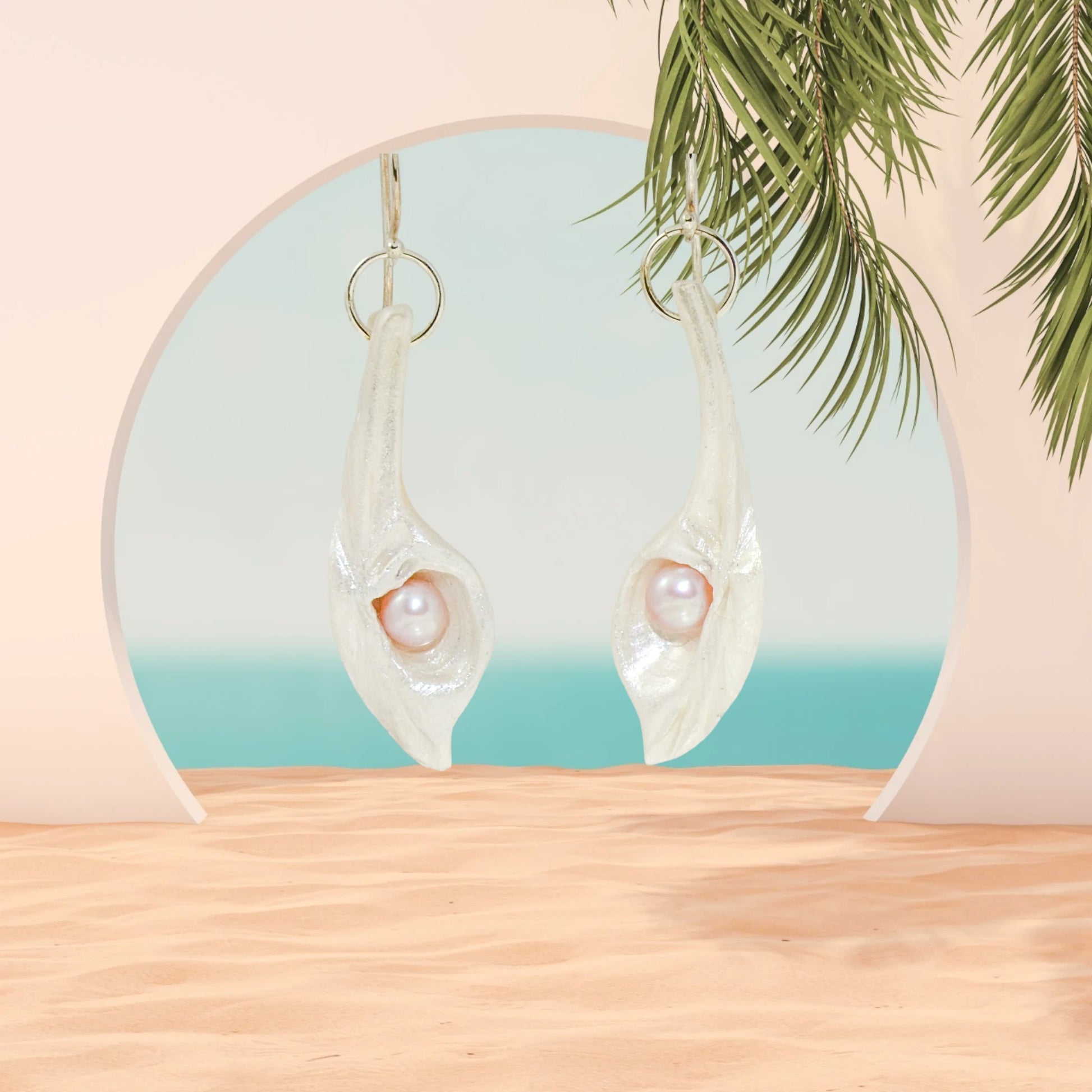 Sea Plume natural seashell earrings with real pink freshwater pearls. The earrings are hanging in an archway leading to the ocean.