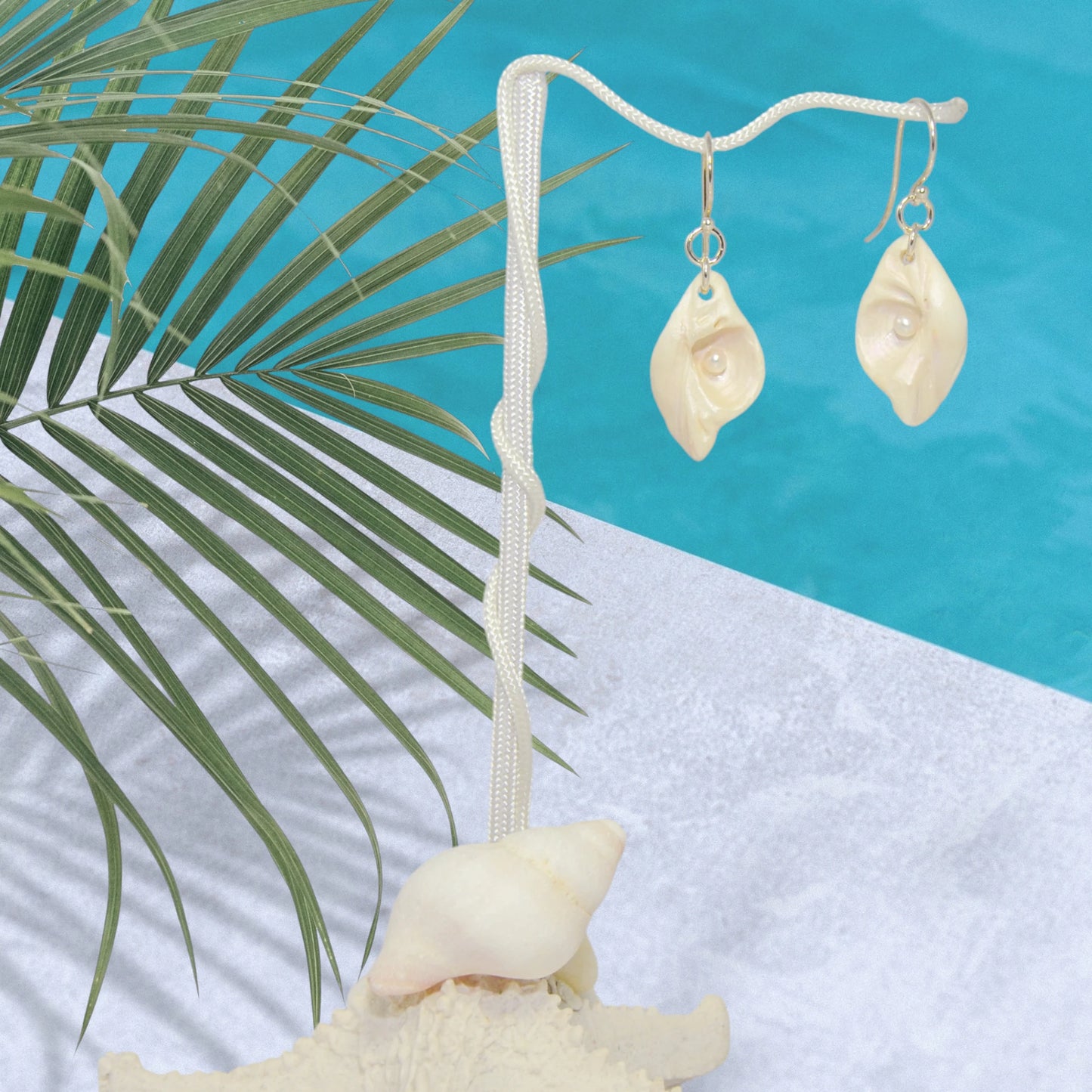 Serenity natural seashell earrings with real baby freshwater pearls. The earrings are hanging on a stand by the pool.