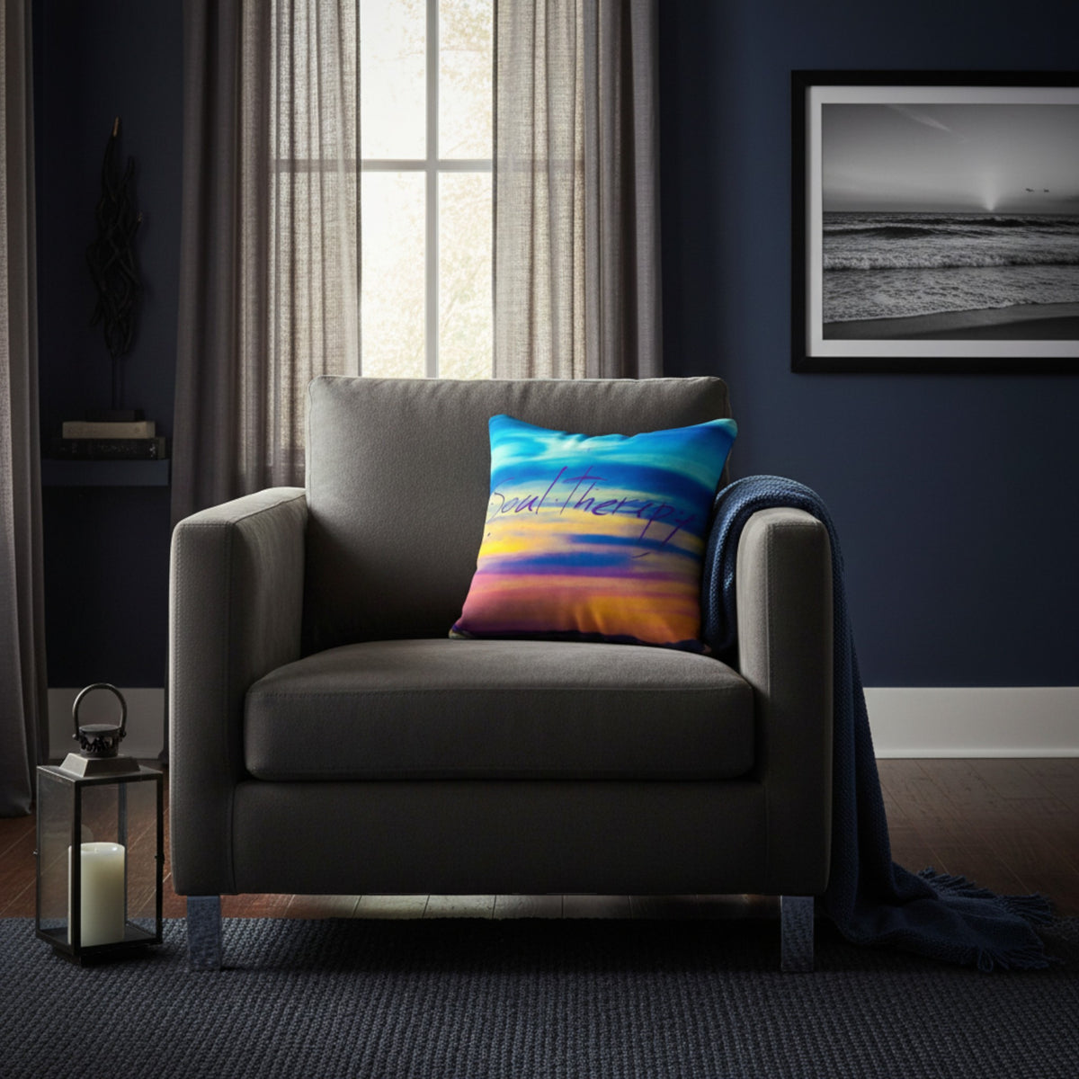 A square throw pillow with a colorful sunset sky print in blue, orange, and yellow, styled on a gray armchair in a dark navy room.