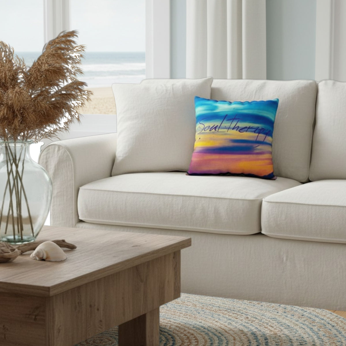A square throw pillow with a colorful sunset design and the words 'Soal Therapy' printed on it, styled on a cream-colored sofa in a bright, modern living room.