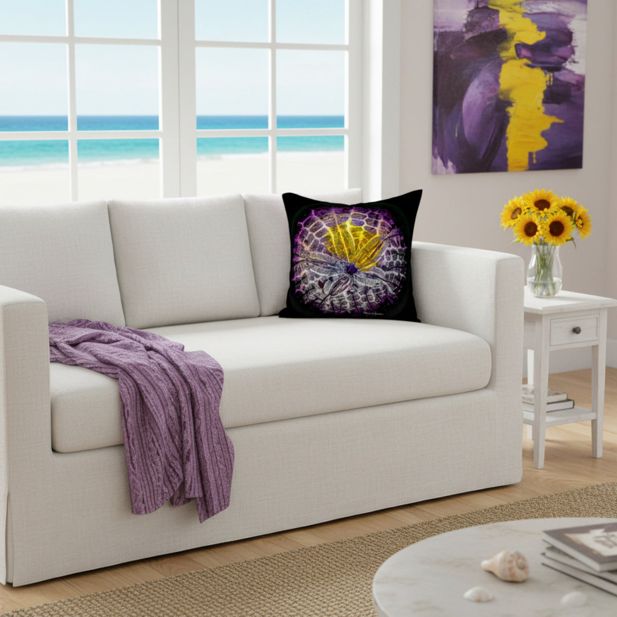 A square black throw pillow featuring a purple and yellow seashell design, styled on a white sofa in a bright, modern living room with an ocean view.