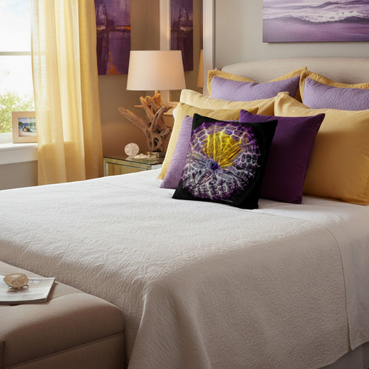 A styled bedroom scene with a bed dressed in white bedding and layered with purple and mustard yellow pillows, including a decorative square throw pillow with a purple seashell motif. The room has warm yellow curtains, a bedside lamp, and matching purple wall art.