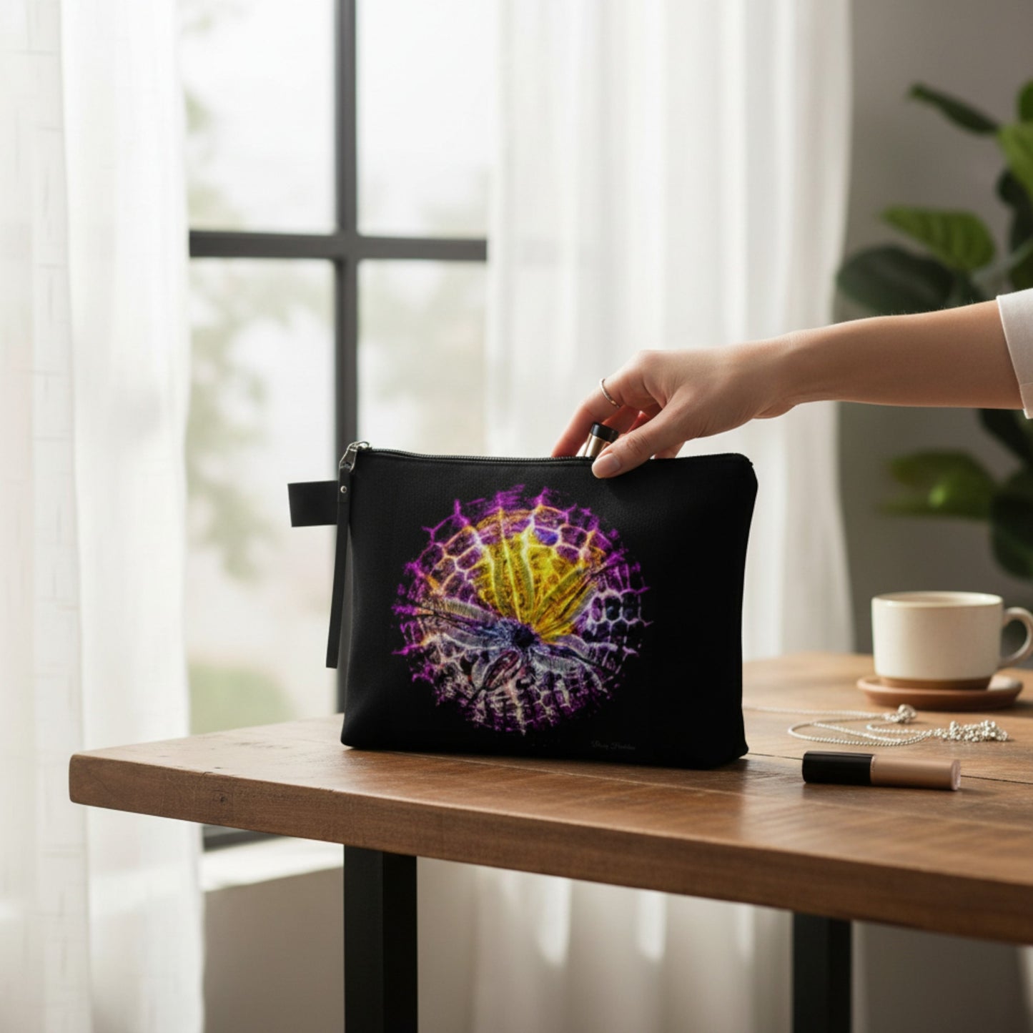 Person holding a black pouch with a colorful sand dollar design on a wooden table.