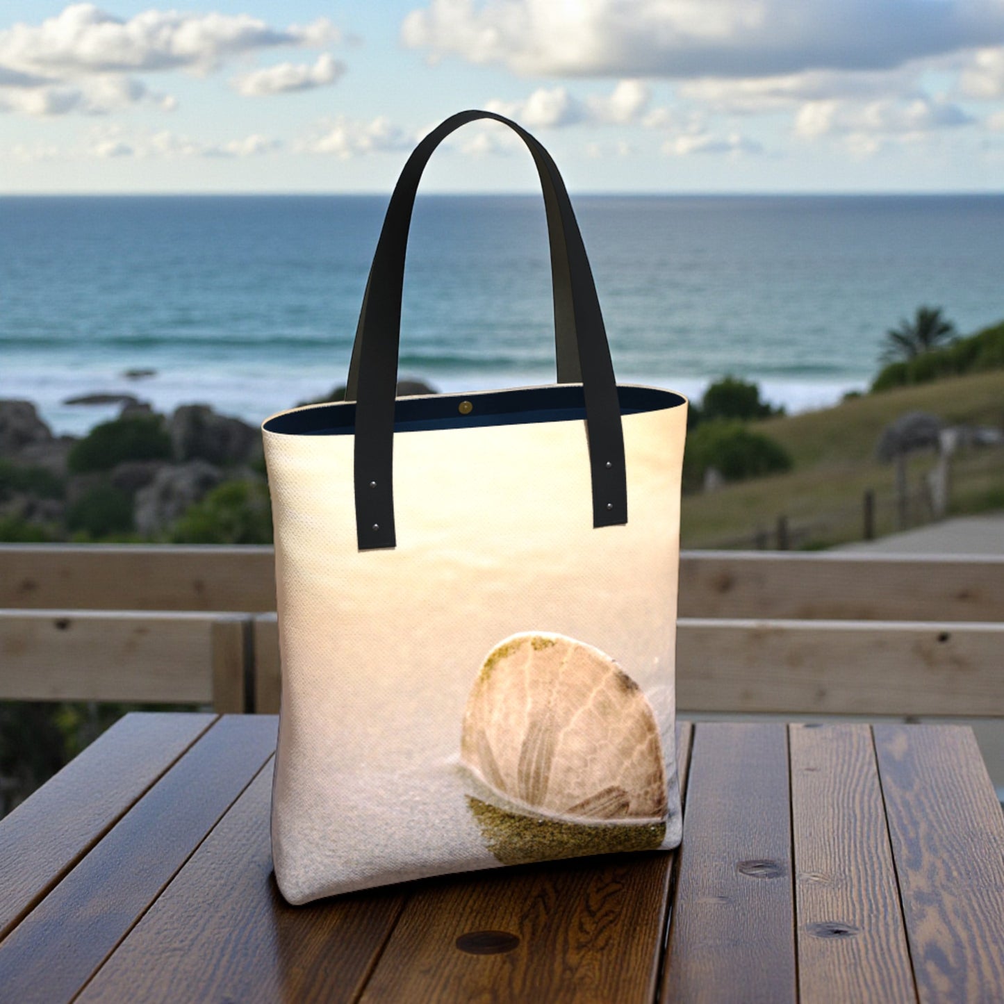 Tote bag with a beach scene design on a wooden table by the ocean.