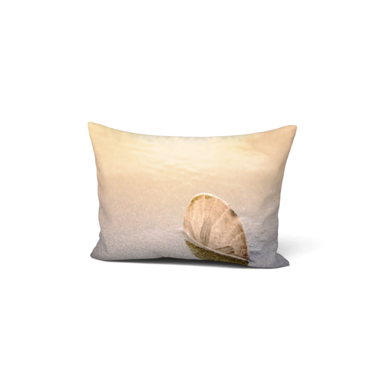 A rectangular throw pillow featuring a photographic print of a seashell on a sandy beach under a warm sky, shown against a plain white background.