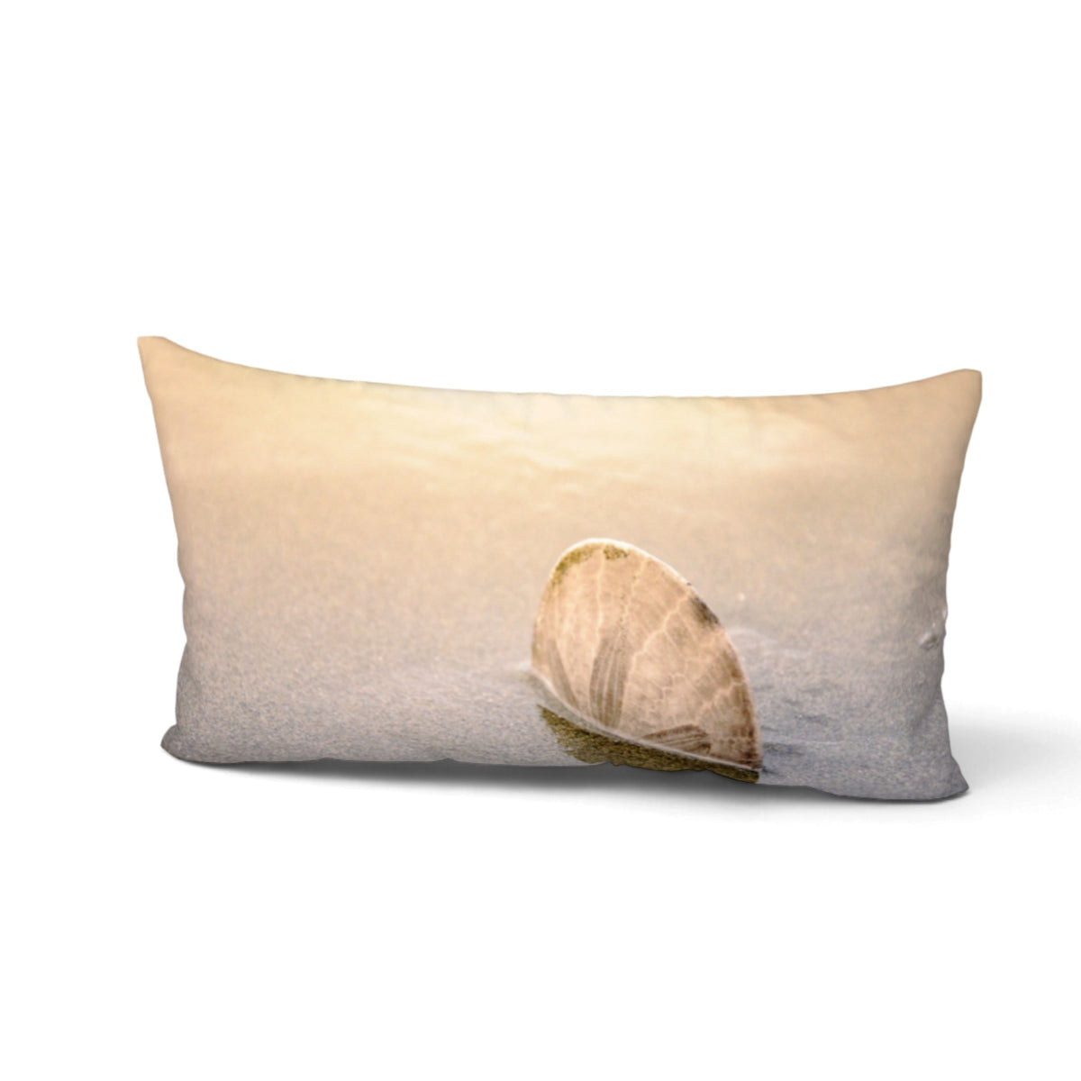 A rectangular lumbar pillow featuring a photographic print of a seashell on a sandy beach at sunset, shown against a plain white background.
